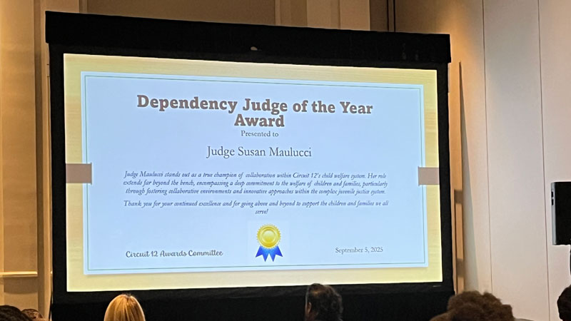 This is an image of a presentation screen in a large meeting that is displaying an award certificate for Judge Maulucci.