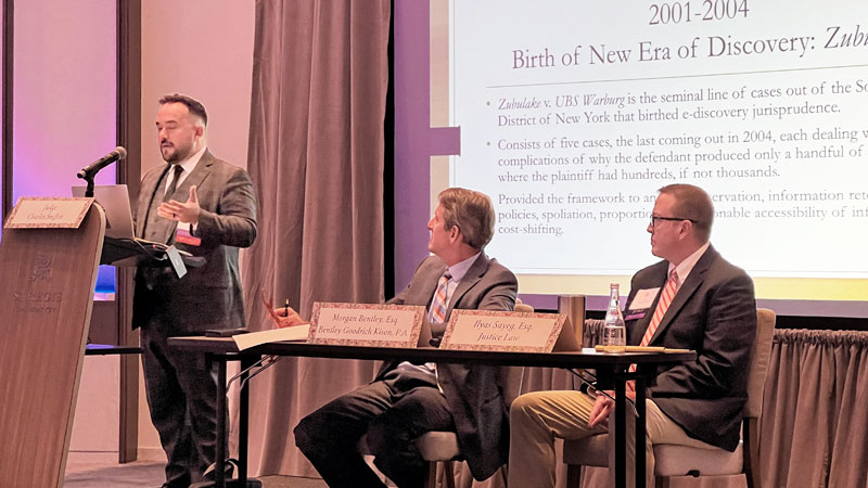 One moderator and two people sit on an elevated stage and speak to an audience.