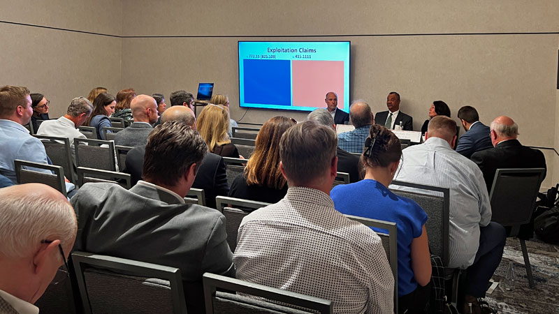 Three people sit at a table in the front of a room and speak to an audience.